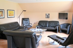 Una sala de estar con un sofá de cuero negro, una mesa de centro de vidrio y un sillón de cuero negro.