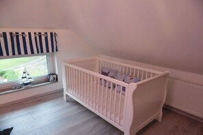 A white crib with a window view, a radiator, and a small sailboat model on the windowsill.