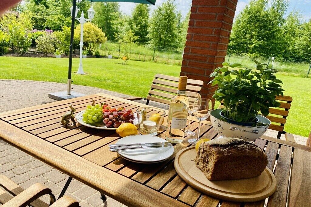 Une table à manger en plein air, avec un pain, une assiette de raisins, une bouteille de vin et une plante en pot.