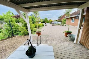 Een overdekt buitengebied met een witte bank, plantenpotten en een fiets.