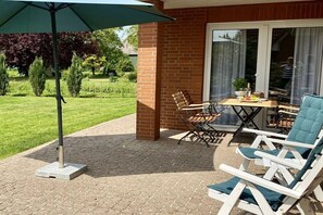 A patio with a table and chairs, a green umbrella, and a brick wall. - Holiday home with 3 bedrooms (Grünendeich)