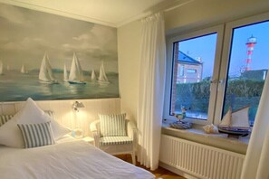 A bedroom with a bed, a chair, a window with a view of a lighthouse, and a mural of sailboats. - Holiday home with 3 bedrooms (Grünendeich)