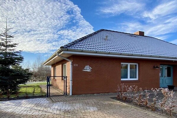 A single-story brick house with a tiled roof, a number '101' on the side, and a gated driveway. - Holiday home with 3 bedrooms (Grünendeich)