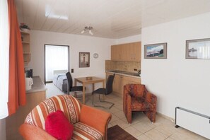 A compact living space with a kitchenette, a dining area, and a sofa with a red pillow. - Holiday apartment with 1 bedroom (Wangerooge)