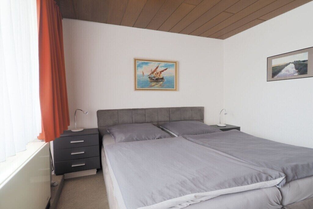 A bedroom with two beds, a nightstand, a lamp, and a window with curtains.