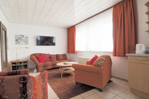 Een woonkamer met een bank, fauteuil, salontafel en een televisie.