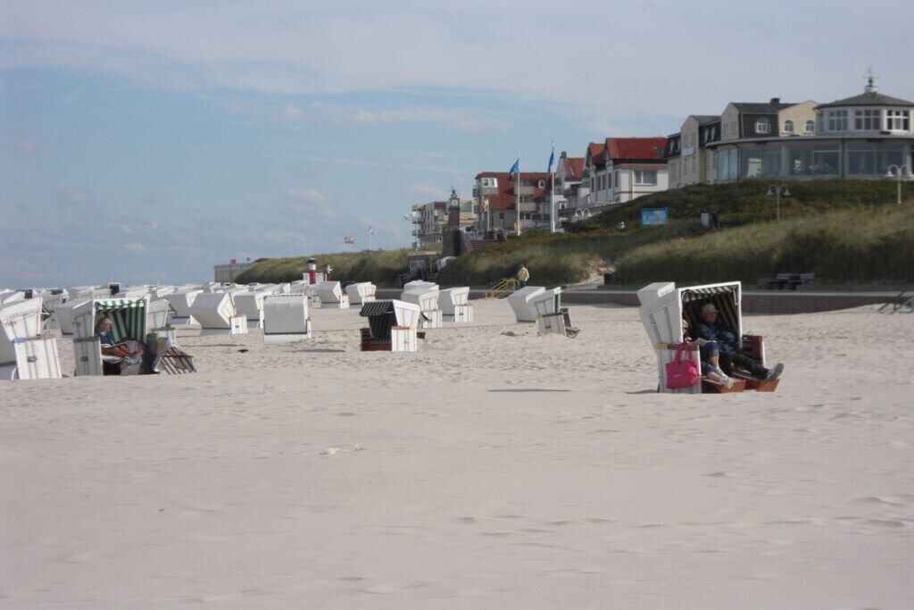 A beach with rows of white beach chairs and umbrellas, a few people, and buildings in the background.