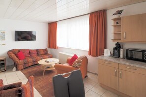 A living room with a sofa, a coffee table, and a TV mounted on the wall. - Holiday apartment with 1 bedroom (Wangerooge)