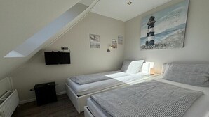 Ein Schlafzimmer mit zwei Betten, einem an der Wand befestigten Fernseher und einem Gemälde eines Leuchtturms.