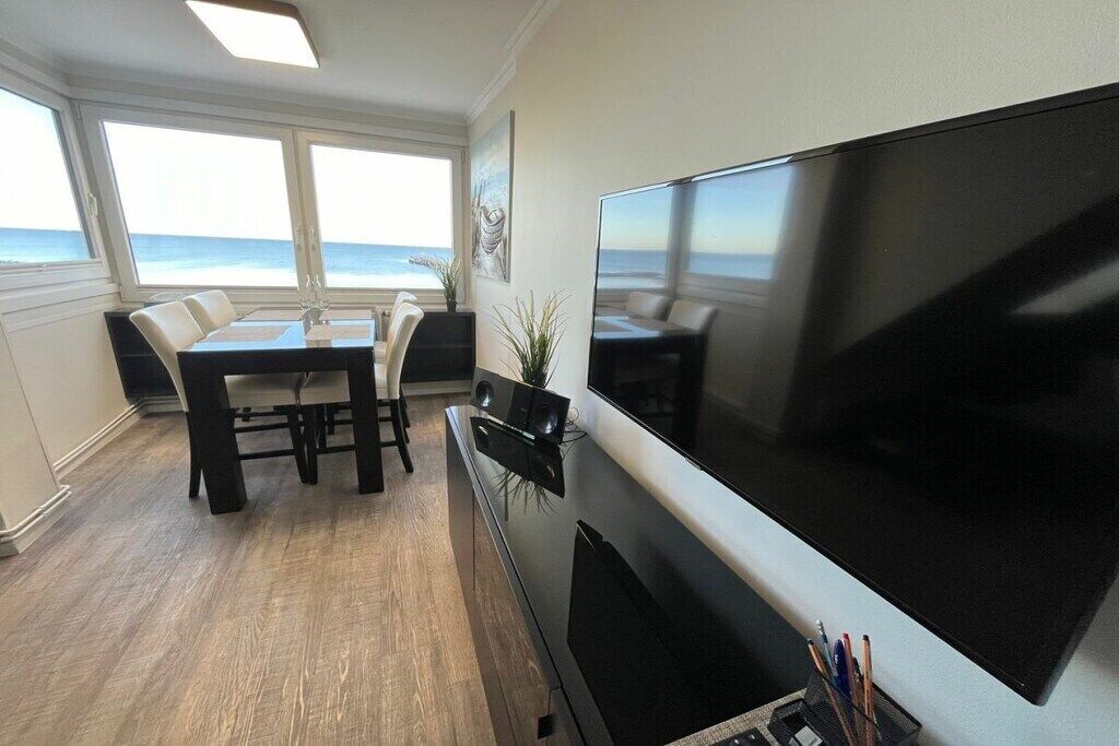 Zona pranzo con vista sull'oceano, una TV a schermo piatto e un tavolo con sedie.