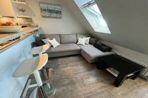 A modern loft apartment with a dining area, a grey sectional sofa, a black coffee table, and a skylight. - Holiday apartment Ostseefee (Schönberger Strand)