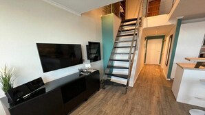 Eine moderne Wohnung mit Treppe, Flachbildfernseher, einer kleinen Küchenzeile und Holzboden.