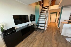 Un apartament modern amb escala, televisió de pantalla plana, petita cuina i terra de fusta.