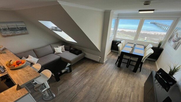 Ein gemütlicher Wohnbereich mit Essplatz, einer Couch, einer kleinen Küche und Meerblick durch große Fenster.