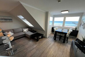 A modern living room with a sofa, coffee table, and dining area. A large window offers a view of the beach. - Holiday apartment Ostseefee (Schönberger Strand)