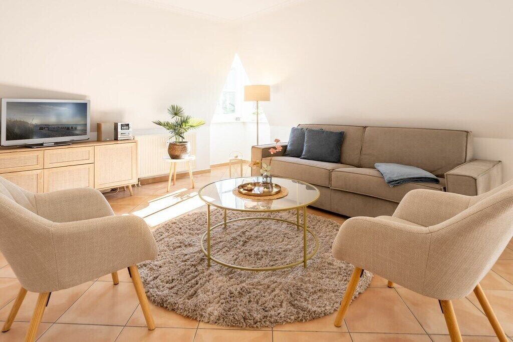 A living room with a sofa, two armchairs, a coffee table, a television, a lamp, and a potted plant.