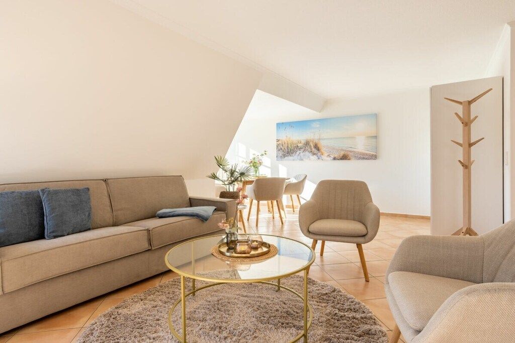 A modern living room with a sofa, armchair, and coffee table. There is a painting on the wall and a plant on the table.