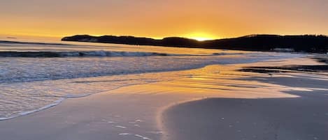 En strand med en solnedgång, vågor och en avlägsen landmassa i horisonten.