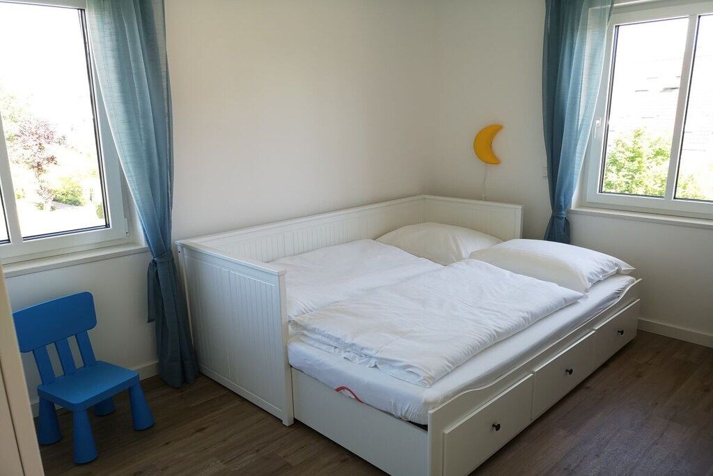 A bedroom with a single bed, a nightstand, a chair, and a window with curtains.