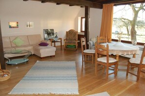 Un salon comprenant un canapé, des fauteuils, une table à manger et donnant sur l’extérieur.