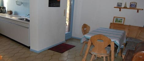 A compact kitchen with a sink, wooden chairs, a table with a striped tablecloth, and a hanging light fixture.