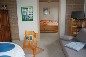 Ein Zimmer mit einem Bett, einem Holzstuhl, einer Couch, einem Fernseher und einem Poster an der Wand.