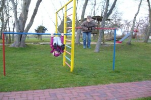 Un parc infantil amb una estructura d'escalada groga i blava, un tobogan vermell i un camí de maó.