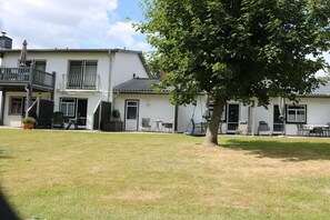 A two-story building with a balcony, a tree in the yard, and outdoor seating. - No. 4 on the Doose farm (Büsum)
