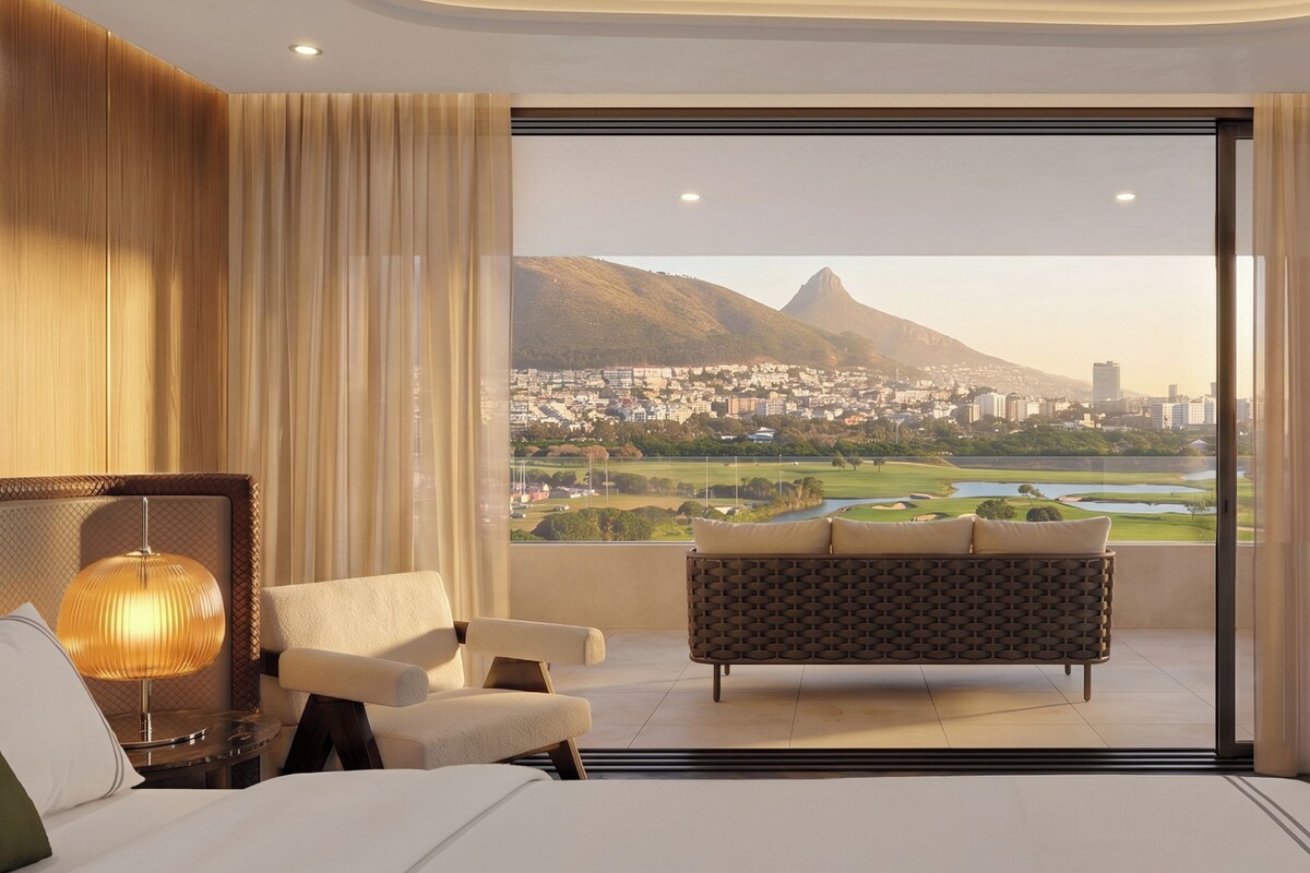 Une chambre d’hôtel avec un grand lit, un canapé, un bureau et une vue sur le paysage urbain et les montagnes.