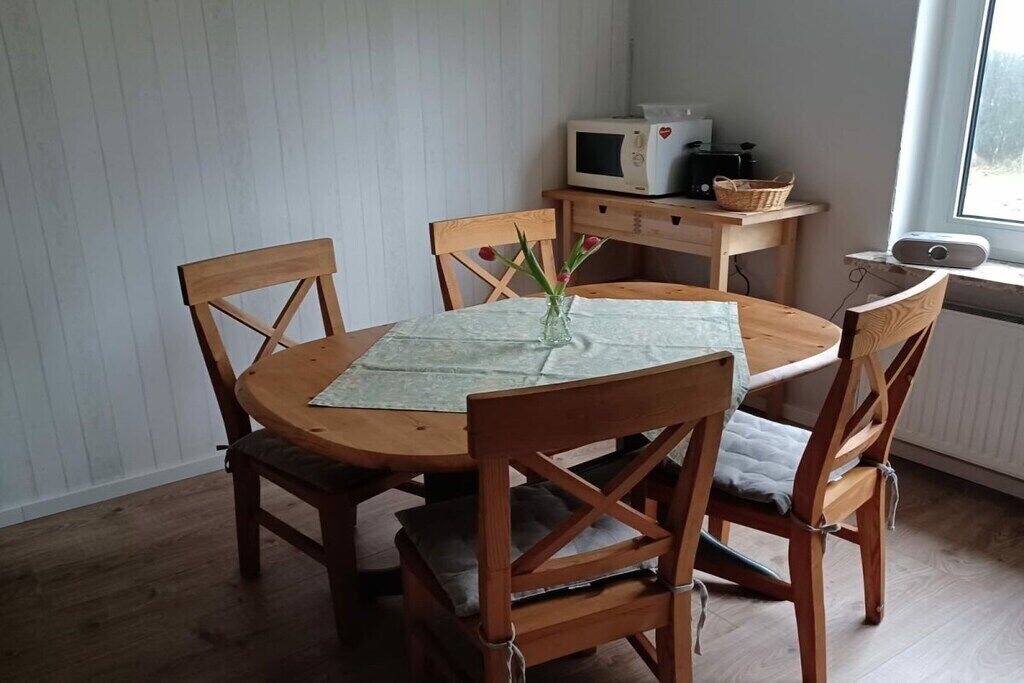 A wooden dining table with four chairs, a white microwave, and a basket on a wooden side table.