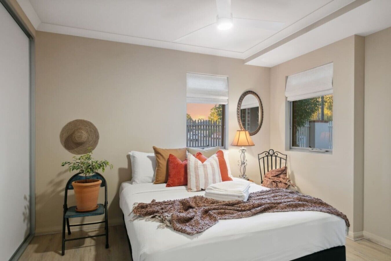 A bedroom with a bed, a potted plant, a lamp, and a view of the outside.