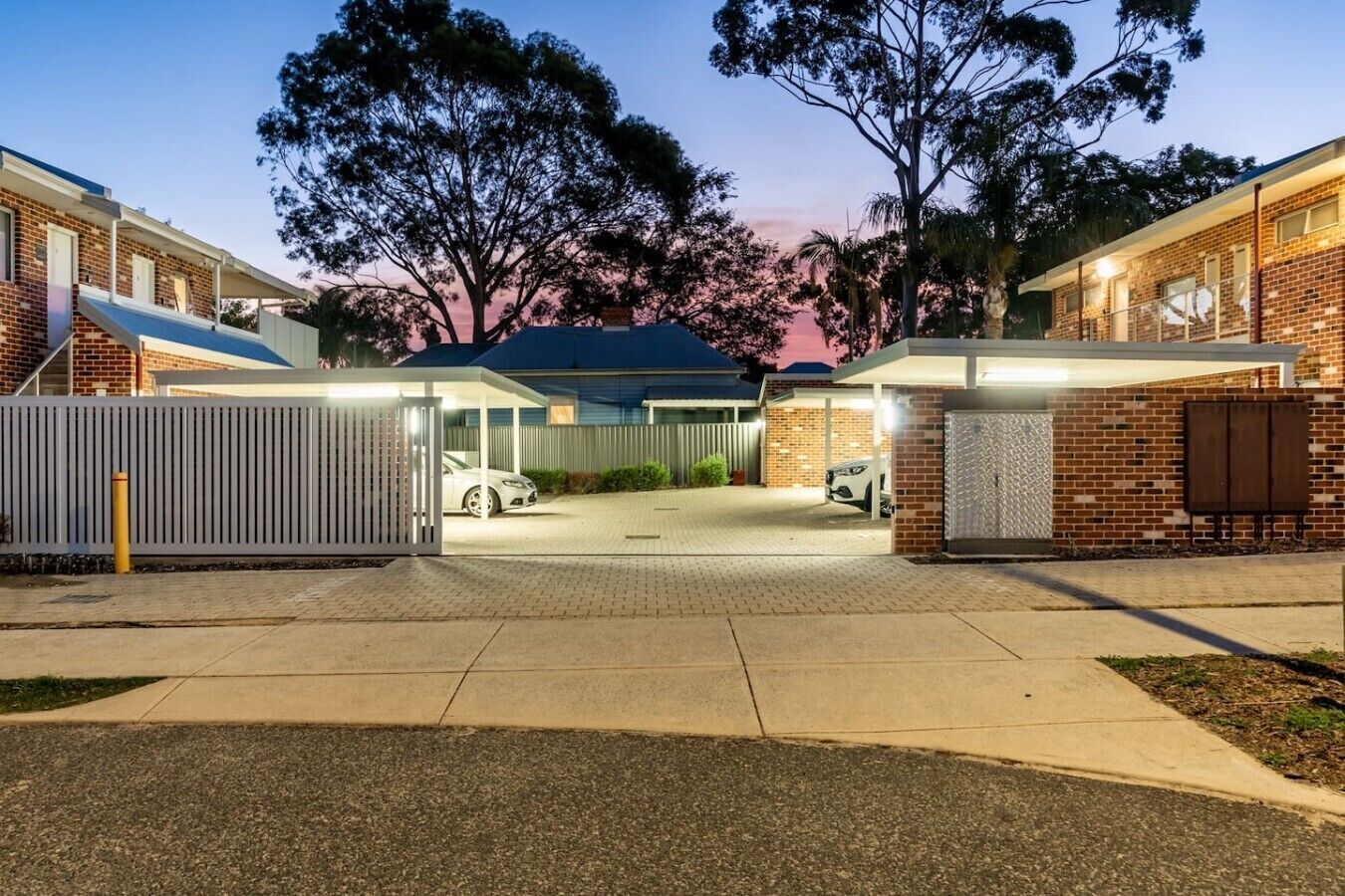 A gated residential area with brick buildings, a covered carport, and a paved driveway.