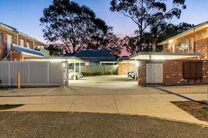 A gated residential area with brick buildings, a covered carport, and a paved driveway.