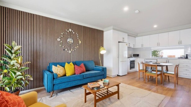 A modern living room with a blue sofa, a wooden coffee table, and a dining area with a wooden table and chairs. - The Tonic | Teal, Timber & Courtyard, Swan Valley (Bassendean)
