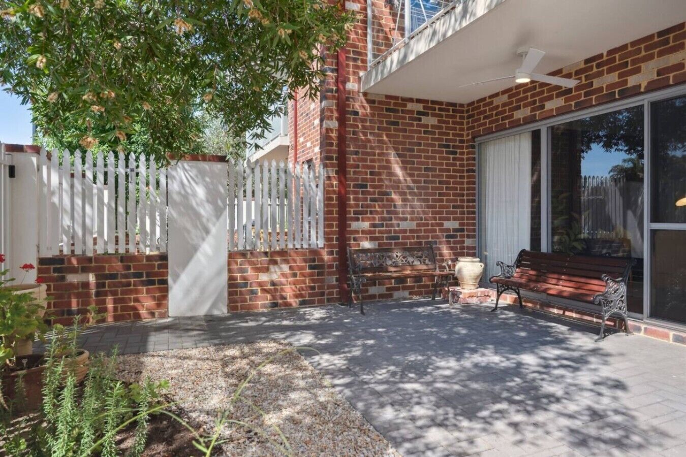 A patio with a brick wall, a white fence, a bench, and a large window.
