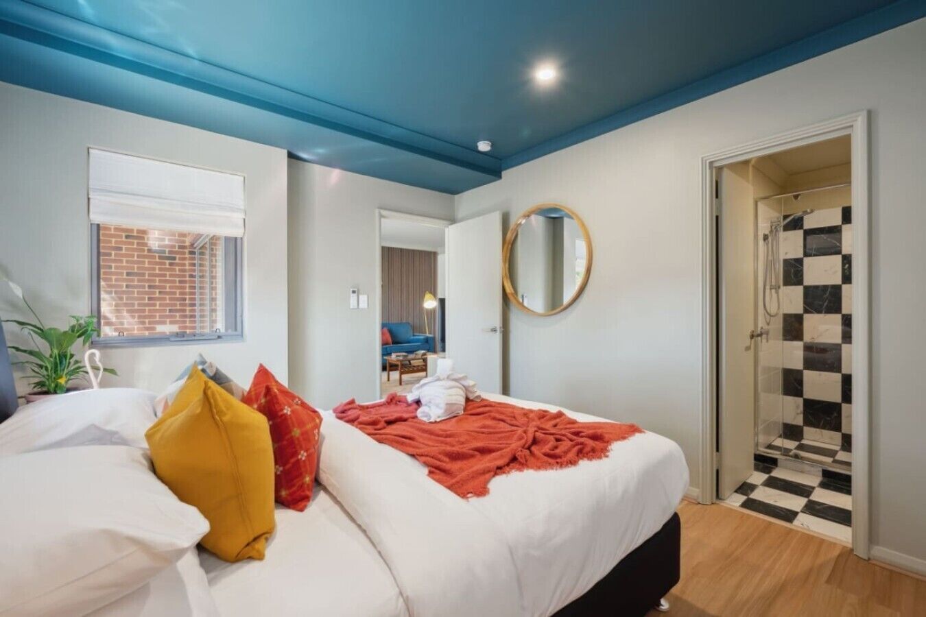 A bedroom with a bed, a window, a mirror, and a shower area.