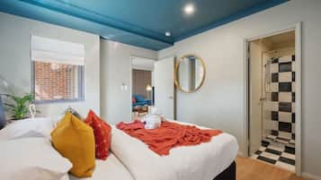 A bedroom with a bed, a window, a mirror, and a shower area.