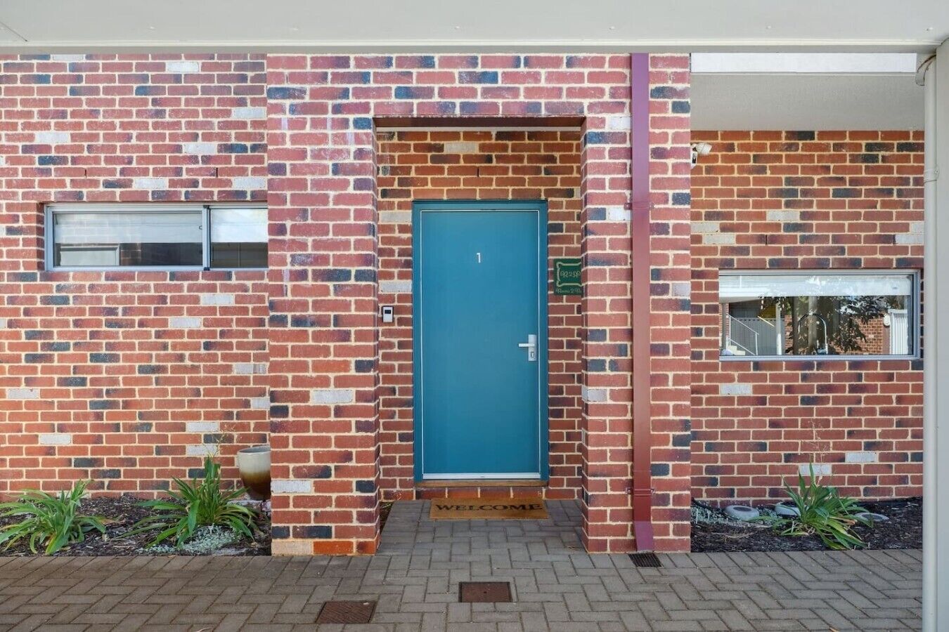 A brick house with a blue door, a small window, and a welcome mat.