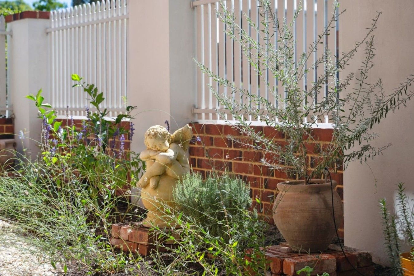 A garden with a statue of a cherub, a large clay pot, and a brick wall.