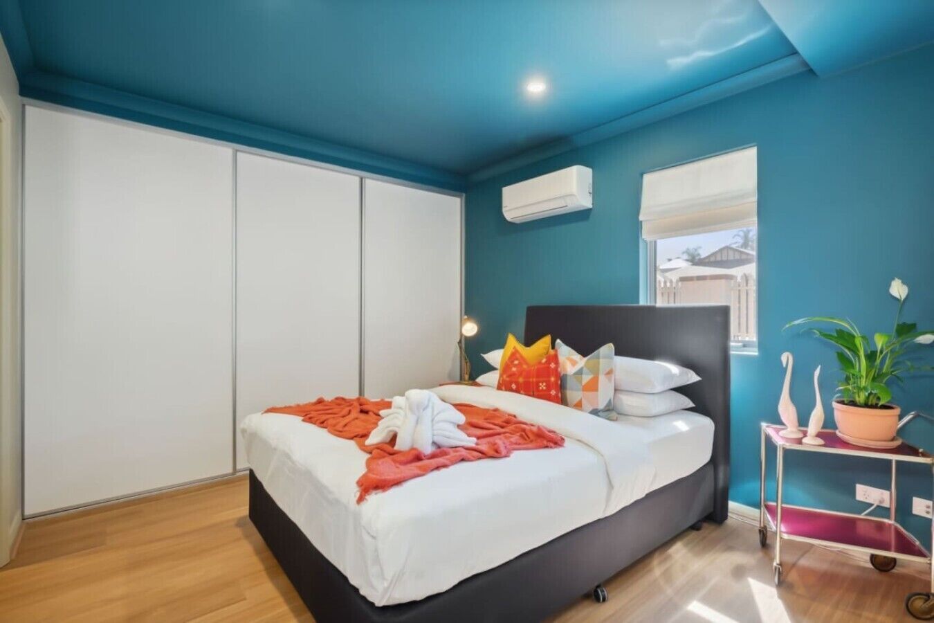 Une chambre à coucher comprenant un lit, une armoire, un appareil de climatisation, une fenêtre et une plante posée sur une table d’appoint.