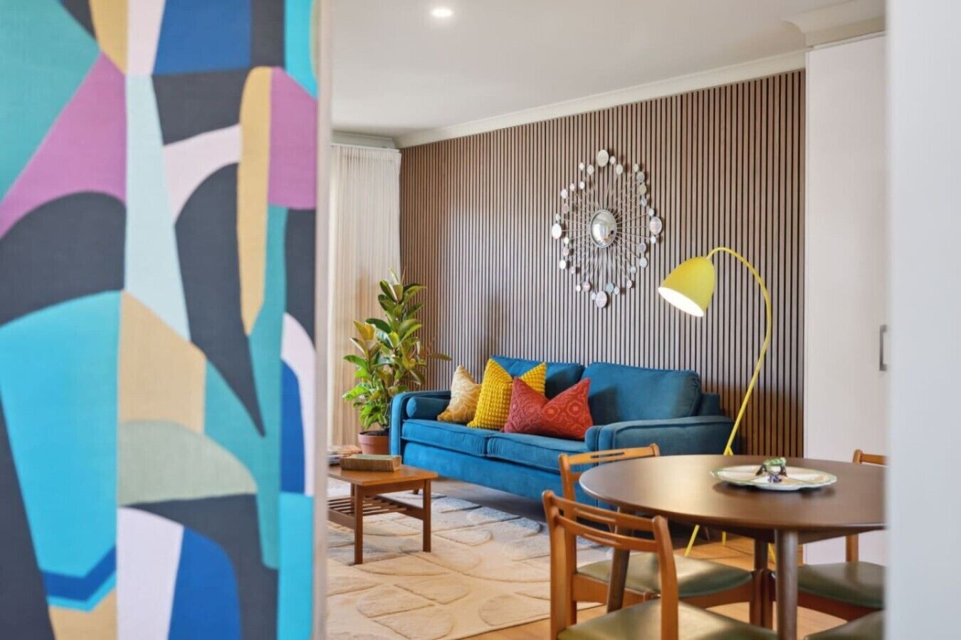 A modern living room with a blue sofa, a round wooden table, and a decorative wall piece.