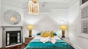 A hotel room with a bed, two bedside lamps, a fireplace, and a wall clock. - The Sapphire House | Art Deco, Arcade, Fenced Yard (Inglewood)