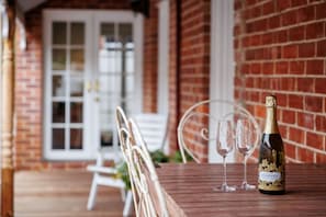 A wooden table with a bottle of wine and two glasses, set against a brick wall with a white door in the background. - The Sapphire House | Art Deco, Arcade, Fenced Yard (Inglewood)