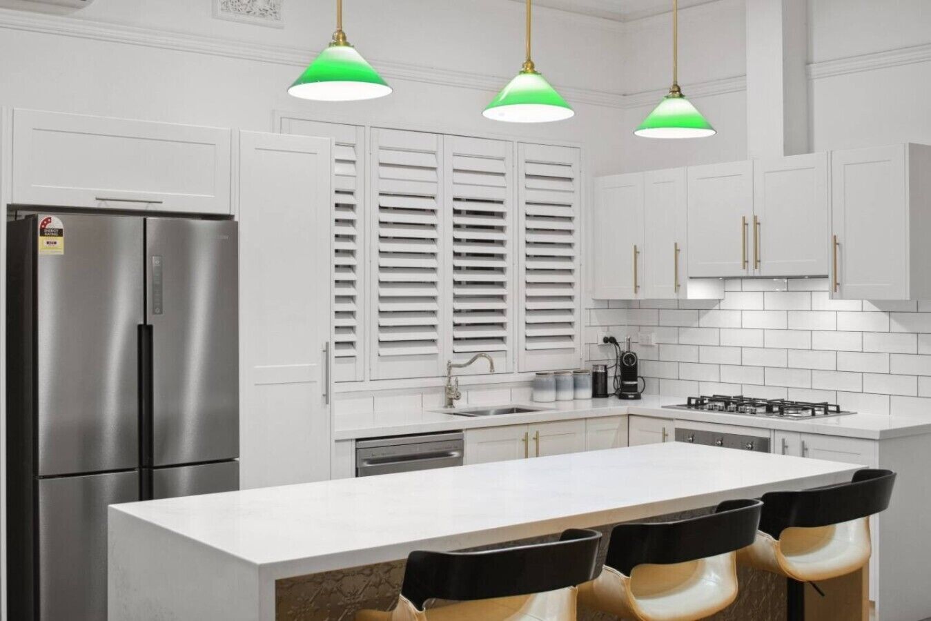 Une cuisine moderne avec des meubles blancs, un réfrigérateur en acier inoxydable, une cuisinière à gaz et un îlot central doté de tabourets de bar.
