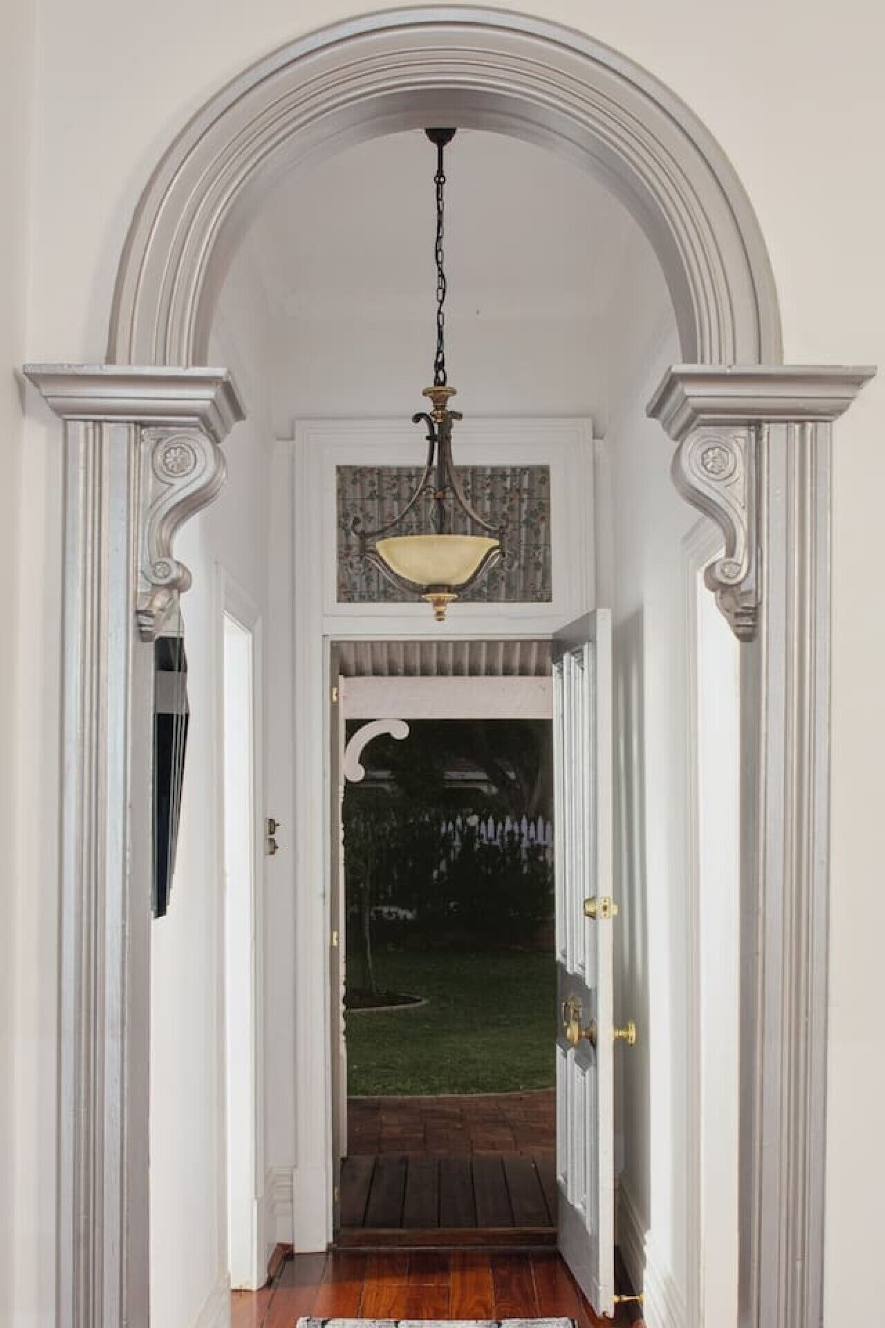 A hallway with a decorative ceiling light fixture, white walls, and a wooden floor.