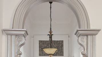 A hallway with a decorative ceiling light fixture, white walls, and a wooden floor.