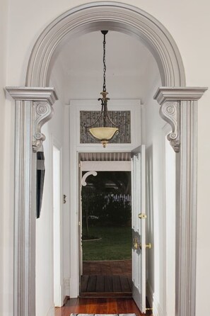 A hallway with a decorative ceiling light fixture, white walls, and a wooden floor.