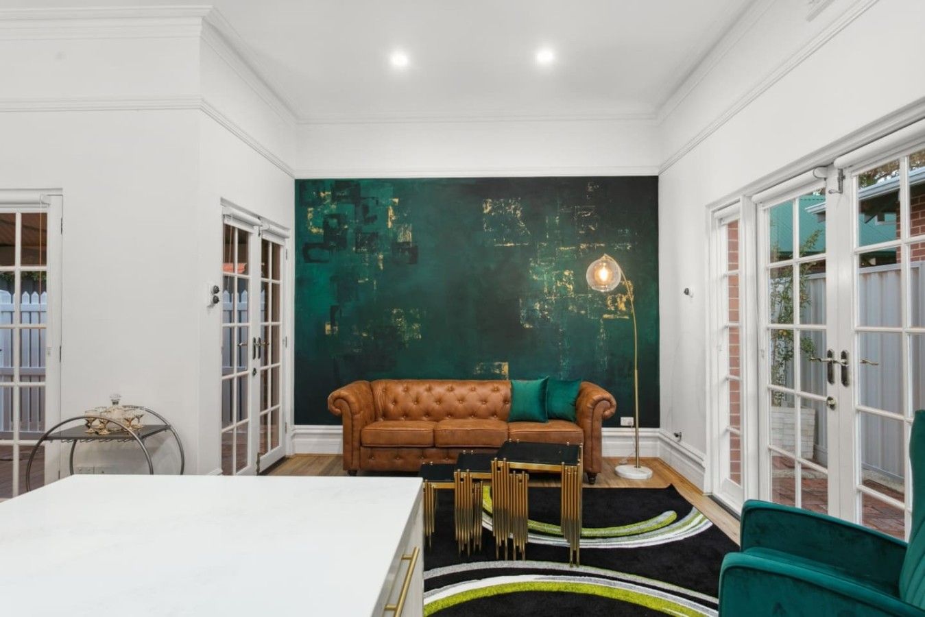 Una habitación con una mesa blanca, un sofá de cuero marrón, un sillón verde y un cuadro abstracto de gran tamaño en la pared.