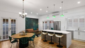 A modern kitchen with a central island, bar stools, a dining table, and a chandelier. - The Sapphire House | Art Deco, Arcade, Fenced Yard (Inglewood)