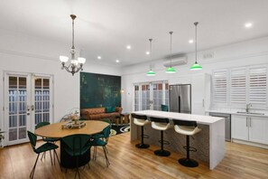 A modern kitchen with a central island, bar stools, a dining table, and a chandelier. - The Sapphire House | Art Deco, Arcade, Fenced Yard (Inglewood)